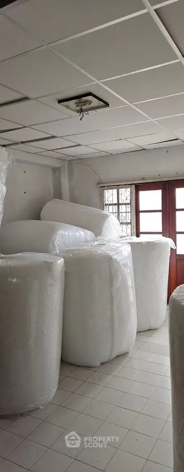 Spacious storage room with large wrapped items and natural light from windows.