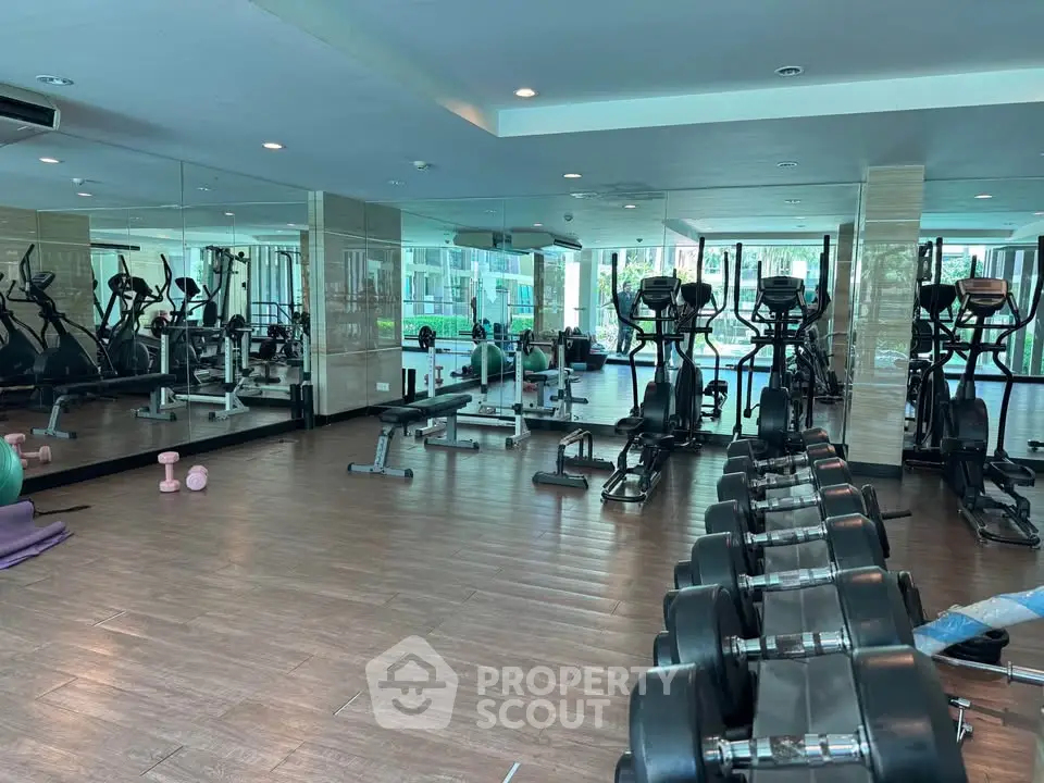 Spacious gym with modern equipment and mirrored walls in luxury apartment complex.
