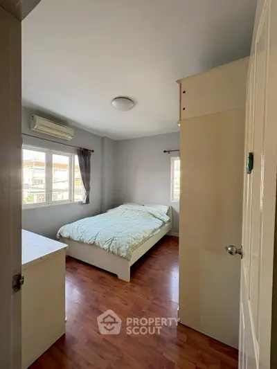 Cozy bedroom with wooden flooring and ample natural light, featuring a comfortable bed and air conditioning.