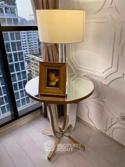 Elegant corner with modern lamp and framed art on glass table, city view from window.