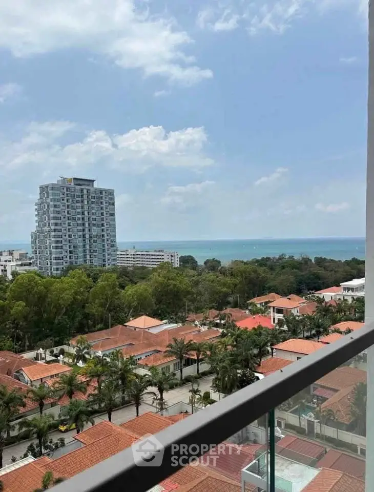 Stunning ocean view from high-rise balcony overlooking lush greenery and red-roofed villas.