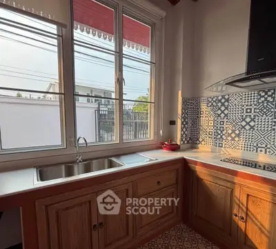 Charming kitchen with patterned backsplash and ample natural light, featuring a sleek sink and wooden cabinetry.