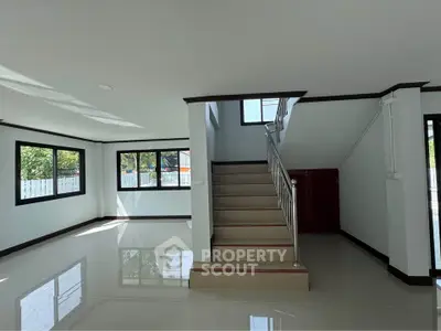 Spacious modern living room with staircase and large windows offering natural light.