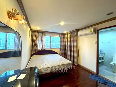 Spacious bedroom with large windows and ensuite bathroom in modern apartment.