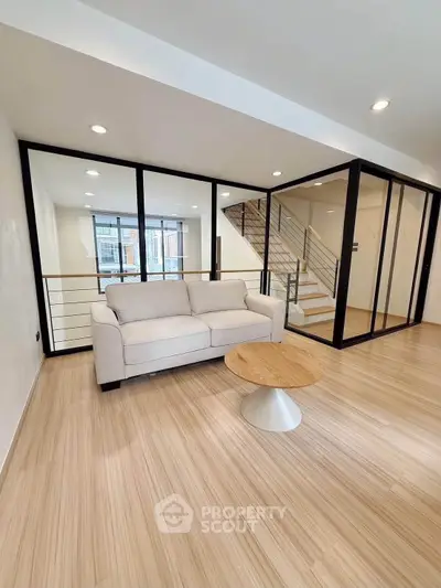 Modern living room with glass walls and wooden flooring, featuring a cozy sofa and stylish coffee table.