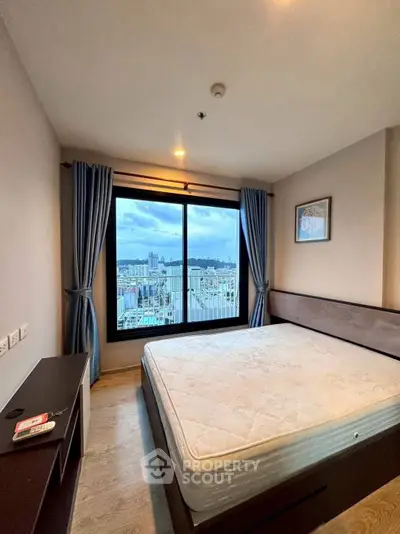 Spacious bedroom with large window offering stunning city view, perfect for urban living.