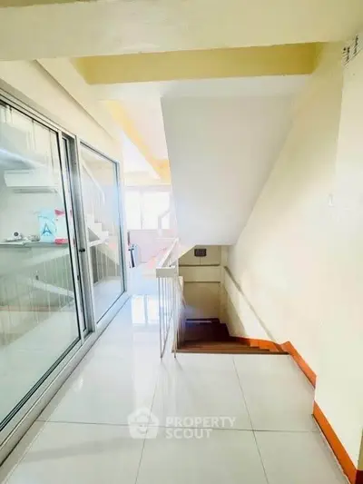 Bright and modern staircase with glass doors leading to a sunlit area, showcasing sleek design and spaciousness.