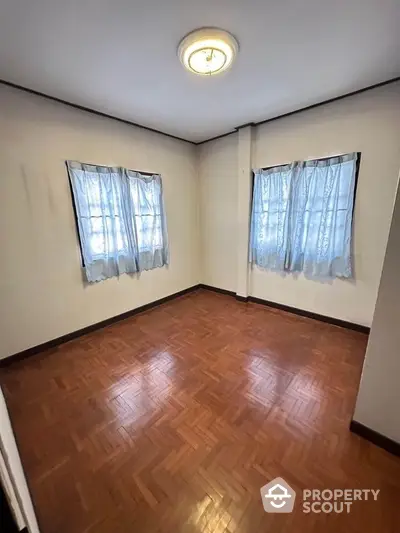 Spacious empty room with wooden flooring and natural light from two windows