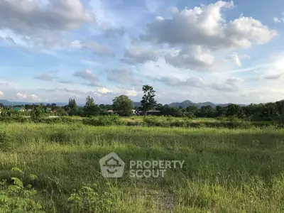 Expansive green field with scenic mountain views under a blue sky, perfect for development.