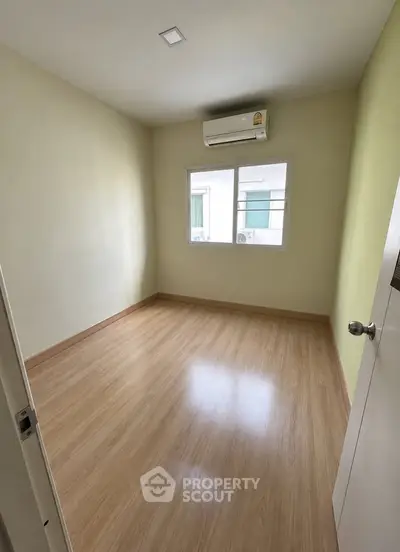 Spacious empty bedroom with wooden flooring and air conditioning, ready for personalization.