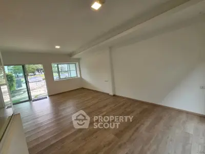 Spacious empty living room with wooden flooring and large windows offering natural light.