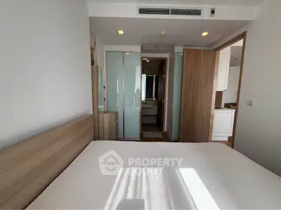 Modern bedroom with wooden accents and ensuite bathroom in a stylish apartment.