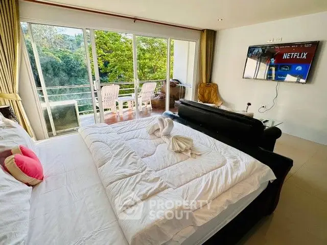 Spacious bedroom with balcony and lush green view, featuring modern TV setup.