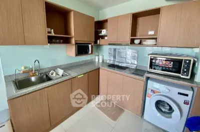 Modern kitchen with wooden cabinets, washing machine, and microwave in compact layout.