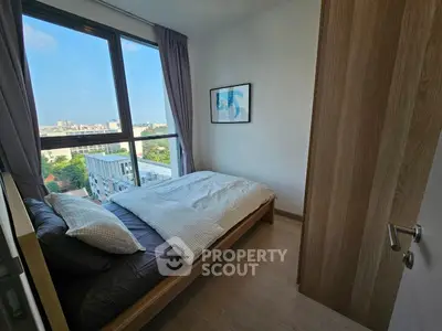 Cozy bedroom with large window offering stunning city view in modern apartment.