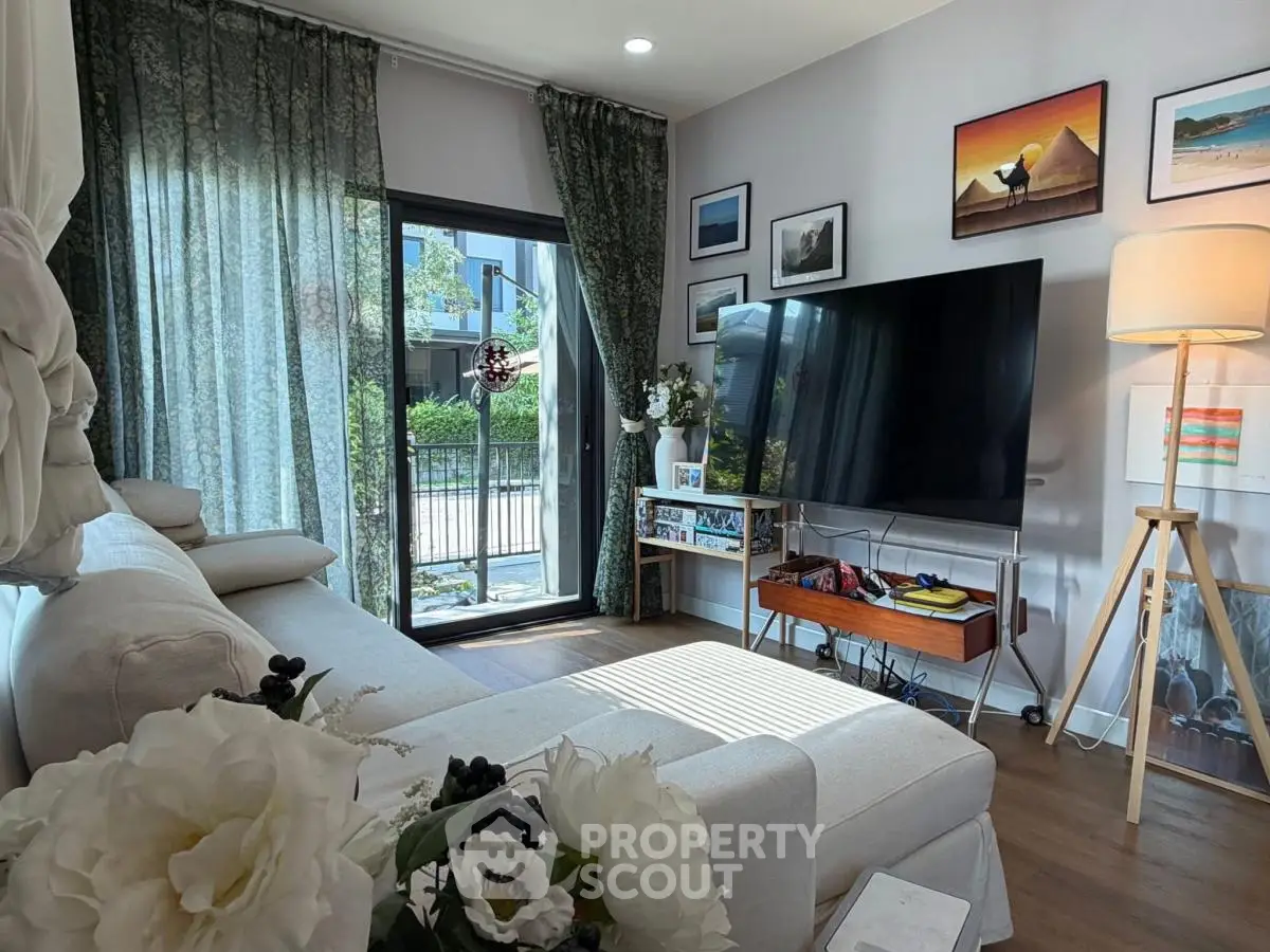 Charming living room with large TV, cozy sofa, and elegant decor, featuring a view of the garden through glass doors.