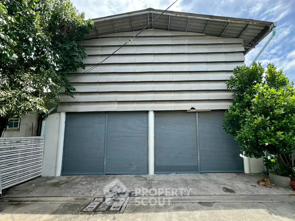 Industrial-style building exterior with large metal shutters and lush greenery