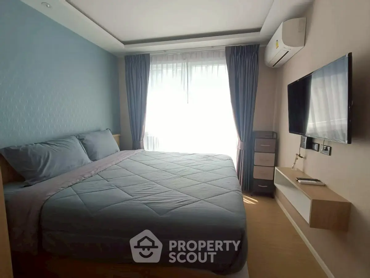 Cozy bedroom with modern decor, featuring a large bed, wall-mounted TV, and natural light from a window.
