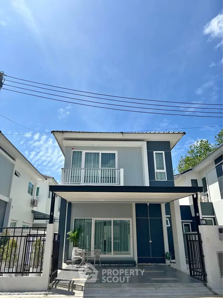 Modern two-story house with balcony and driveway under clear blue sky.