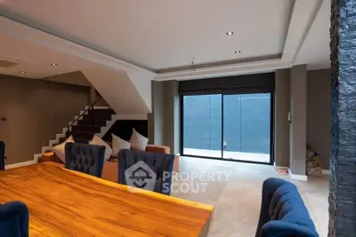 Spacious modern living room with elegant dining area and staircase, featuring plush seating and large windows.