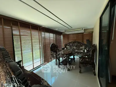 Luxurious living room with ornate wooden furniture and large windows with blinds.