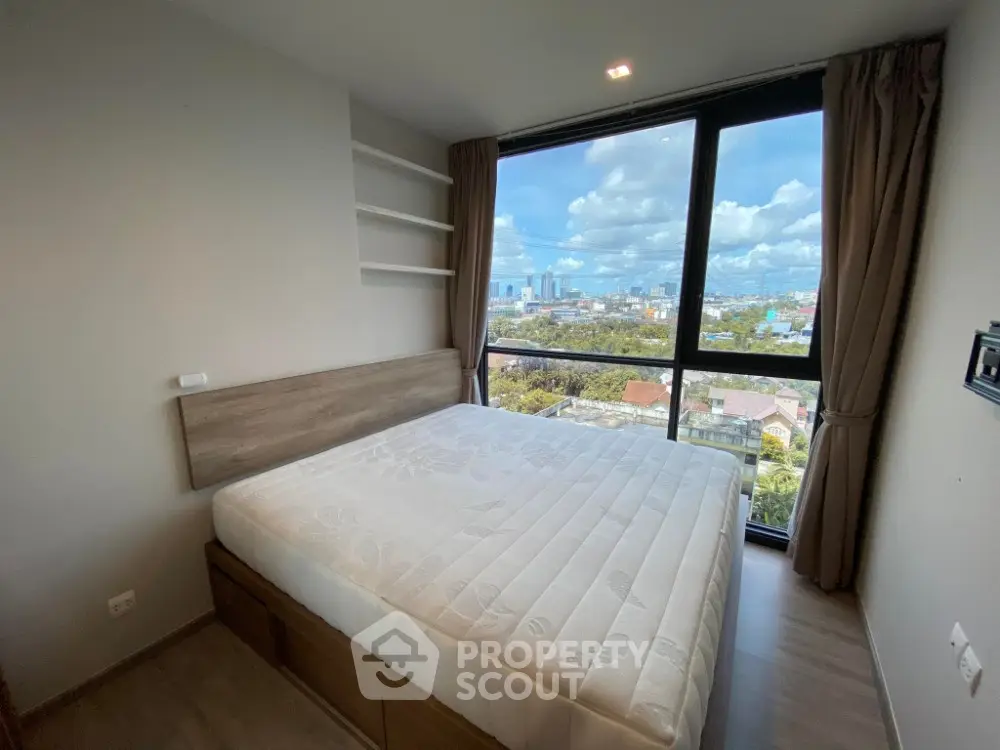 Modern bedroom with large window offering stunning city view, featuring built-in shelves and cozy bed.