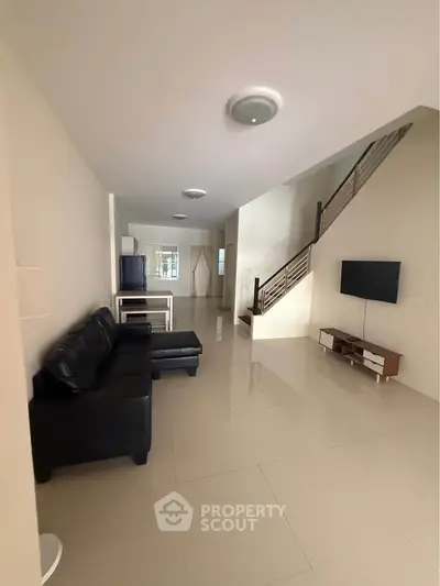 Spacious modern living room with sleek black sofa and wall-mounted TV, featuring elegant staircase design.