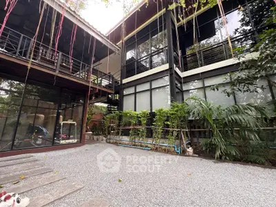 Modern architectural home with large windows and lush greenery in a serene setting.