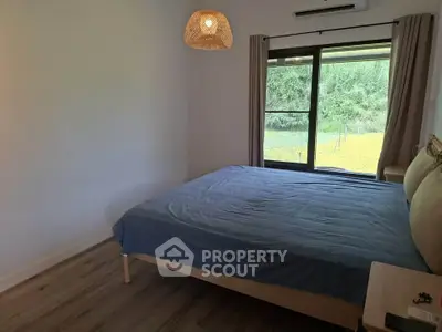 Cozy bedroom with large window and modern decor overlooking lush greenery.