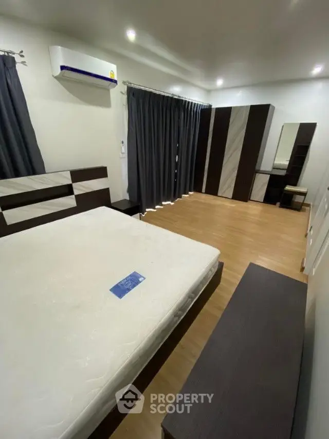 Spacious bedroom with modern design, featuring a large bed with a fresh mattress, sleek dark wardrobes, and elegant black curtains complementing the neutral color palette.