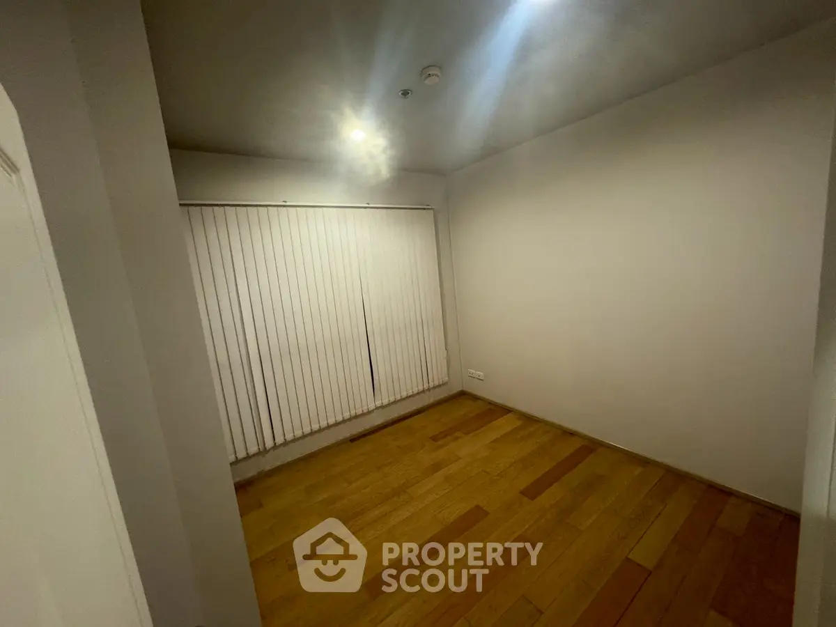 Spacious empty room with wooden flooring and vertical blinds, ideal for customization.