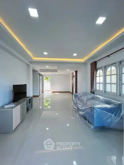 Spacious modern living room with sleek design and natural light, featuring a covered sofa and TV setup.