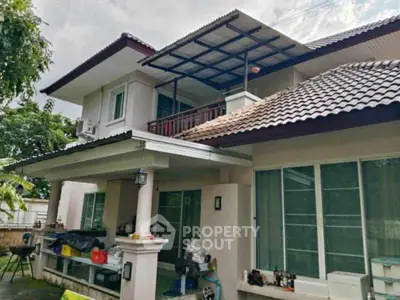 Charming two-story house with a spacious balcony and tiled roof, surrounded by lush greenery.