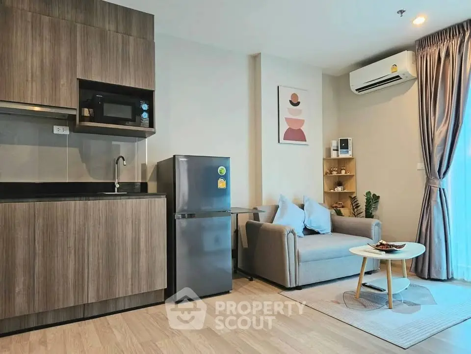 Modern living room with kitchenette, featuring sleek cabinetry, cozy sofa, and natural light from large window.