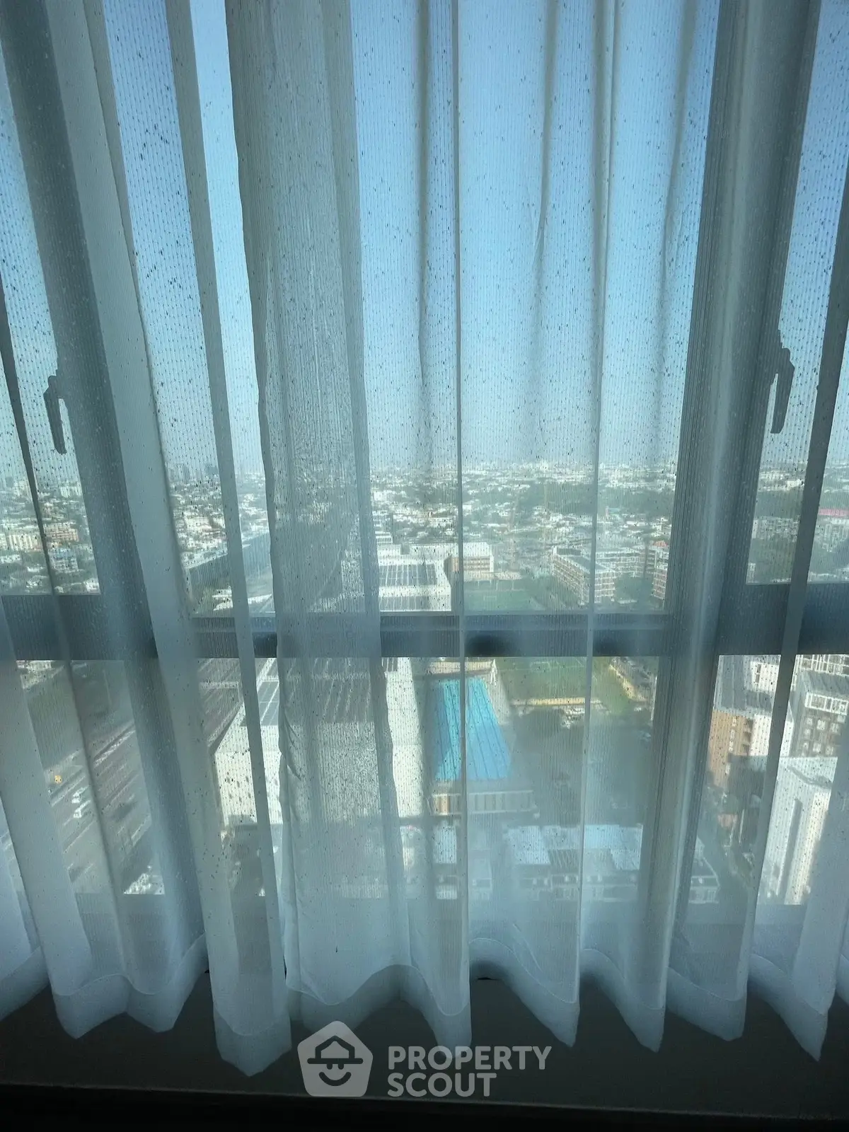 Stunning cityscape view through elegant sheer curtains from a high-rise apartment window.
