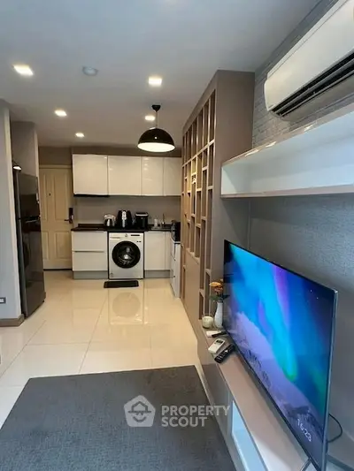 Modern living room with sleek design, featuring a wall-mounted TV, air conditioning, and a compact kitchen area.