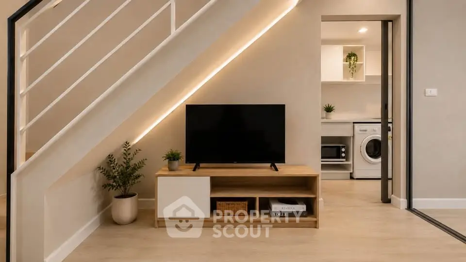 Modern living room with sleek TV stand and view into stylish kitchen with washing machine.