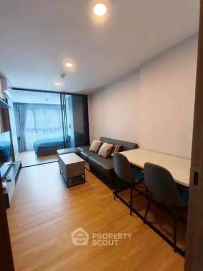 Modern open-plan living room with wooden flooring and cozy seating area, leading to a stylish bedroom.
