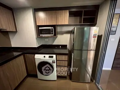 Modern kitchen with sleek appliances and wood cabinetry, featuring a washing machine and stainless steel fridge.