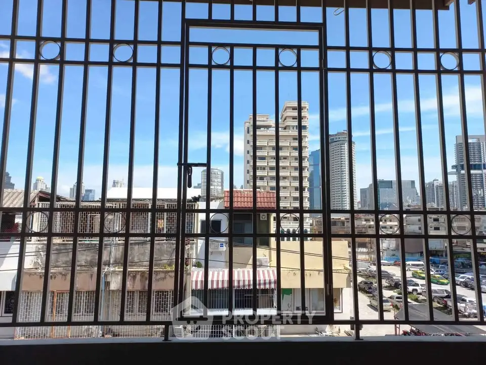 Urban cityscape view from a balcony with metal railing, showcasing high-rise buildings.