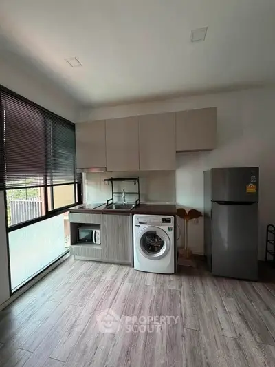 Modern kitchen with washing machine, microwave, and fridge in sleek apartment.