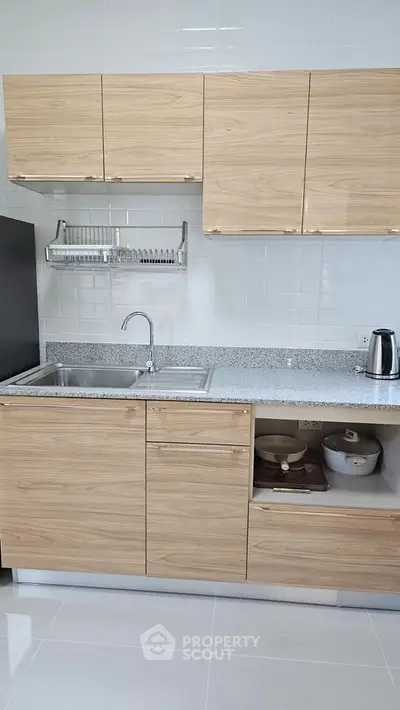 Modern kitchen with sleek wooden cabinets and granite countertop, featuring a stainless steel sink and electric kettle.