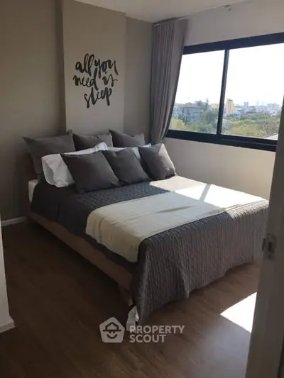 Cozy bedroom with stylish decor and large window offering natural light and city view.