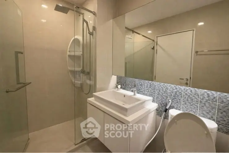 Modern bathroom with glass shower and sleek vanity in contemporary apartment.