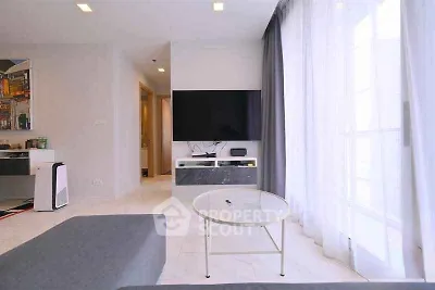 Modern living room with large TV and natural light through sheer curtains.