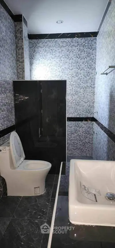 Modern bathroom with sleek black and gray tiles, featuring a toilet and sink.