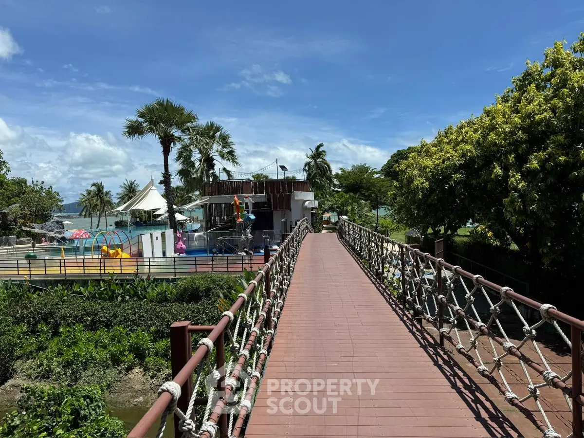 Scenic view of a resort-style pool area with lush greenery and a wooden bridge.