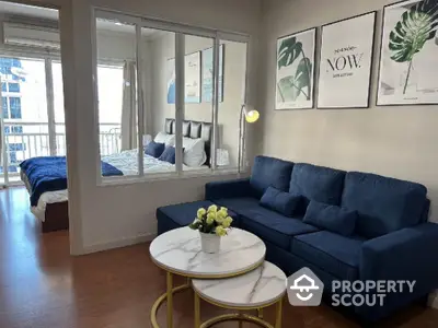 Modern living room with blue sofa and stylish decor adjacent to a cozy bedroom with balcony view.