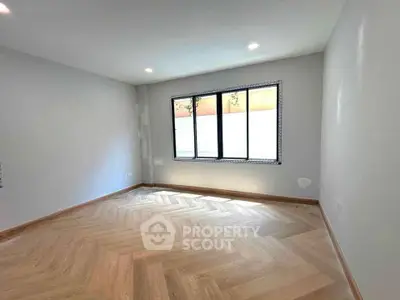 Spacious empty room with elegant herringbone wood flooring and large window.