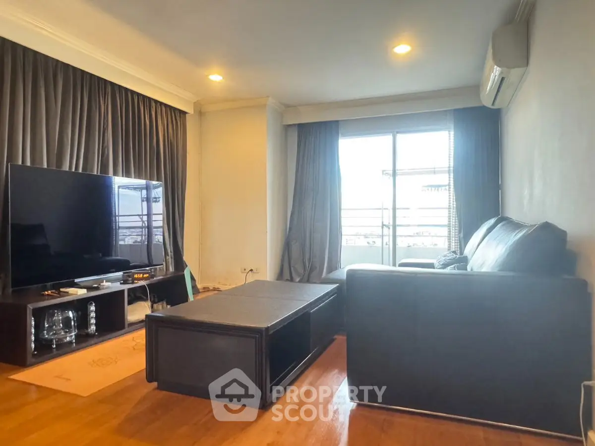 Spacious living room with modern furniture and large TV, featuring a balcony view.